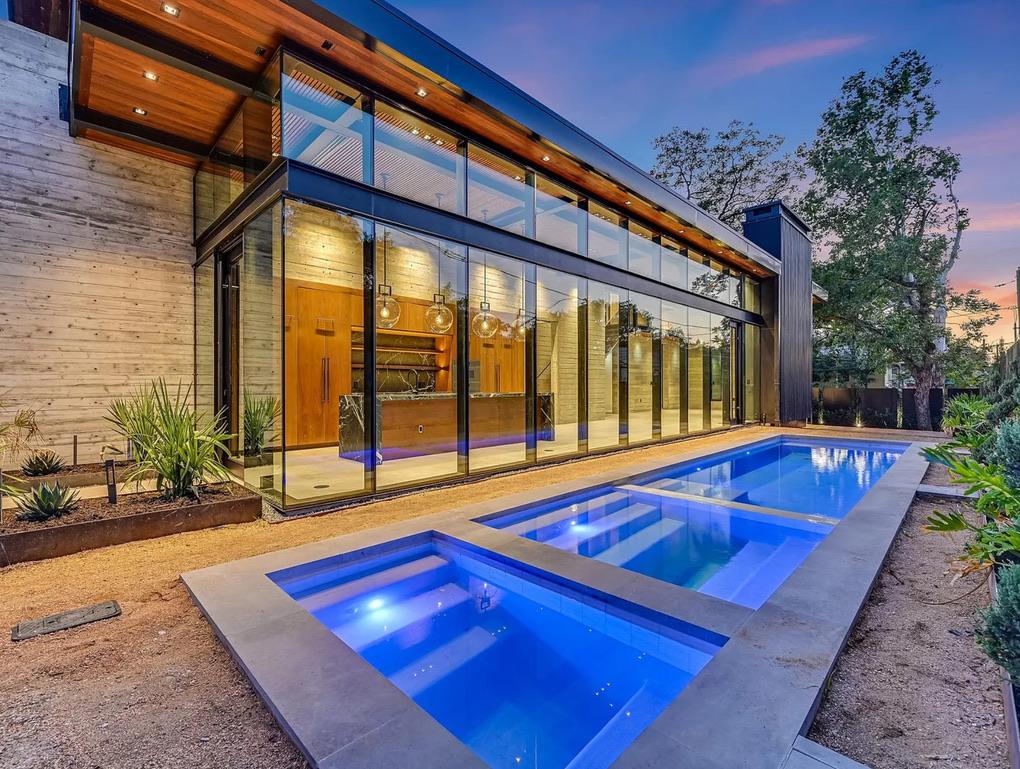 Two story glass curtain wall facing a pool at dusk